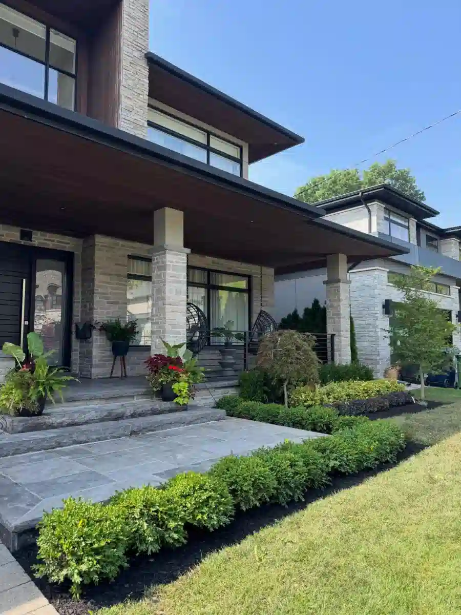 Modern front yard with a broad green lawn, low shrubs, clean paving, and simple landscaping around the house.
