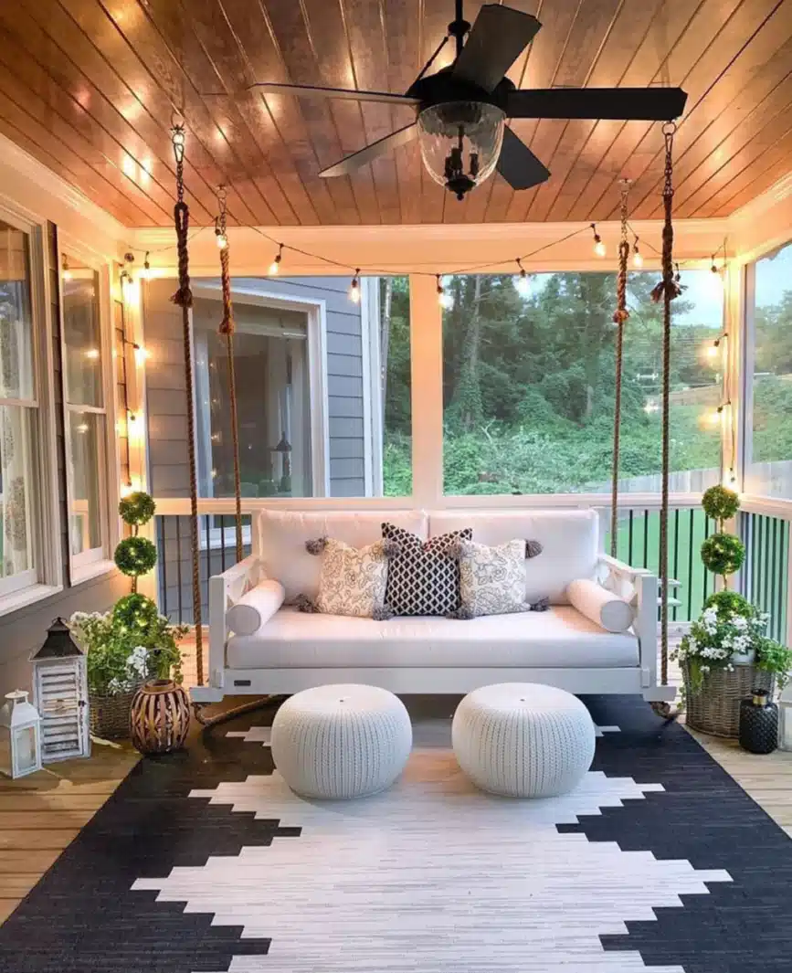 Enclosed farmhouse porch with cushioned seating, a large rug, low coffee tables, a ceiling fan, and warm wood ceiling