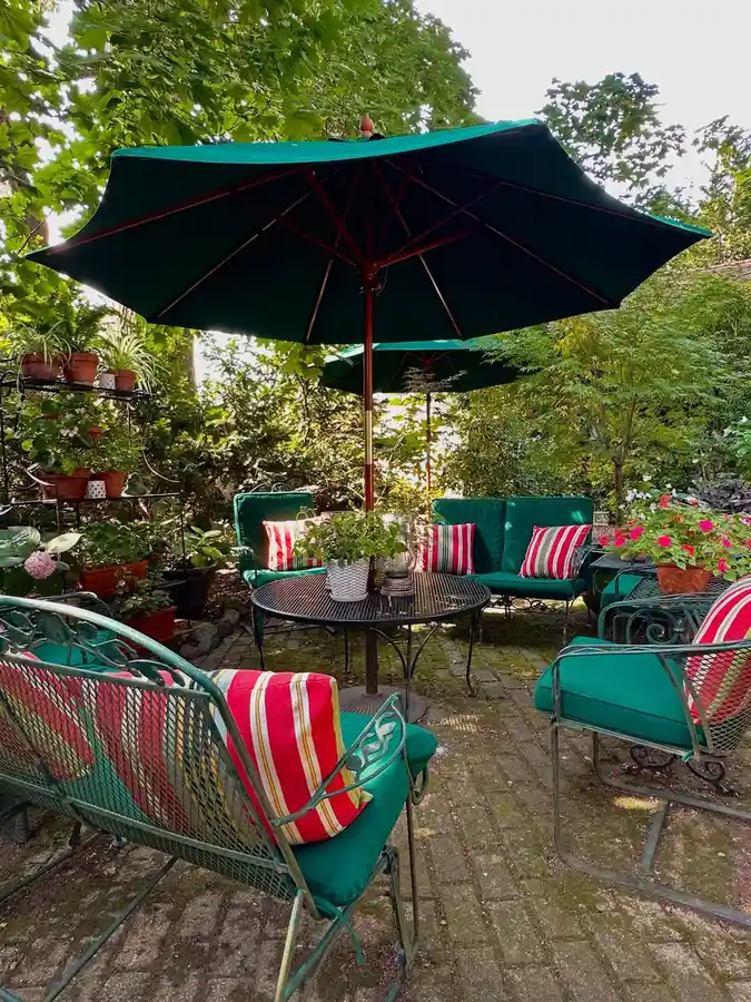 Garden patio with deep green umbrellas, matching outdoor furniture, red-and-white striped cushions, and leafy plants