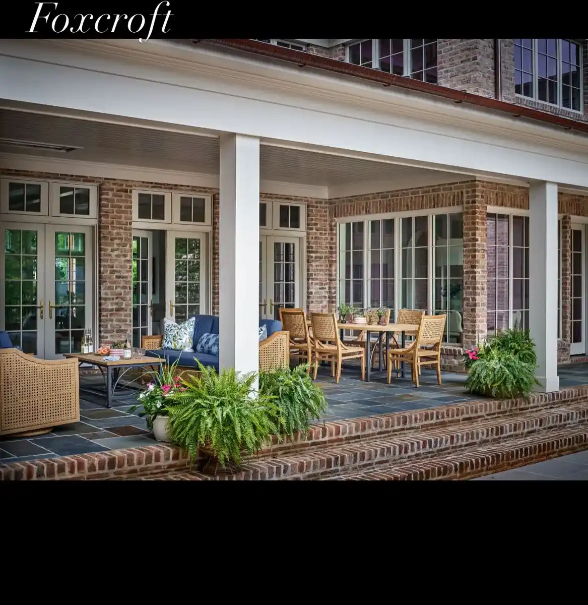 Large covered porch with separate dining and seating areas, wood columns, plants, and classic architecture.