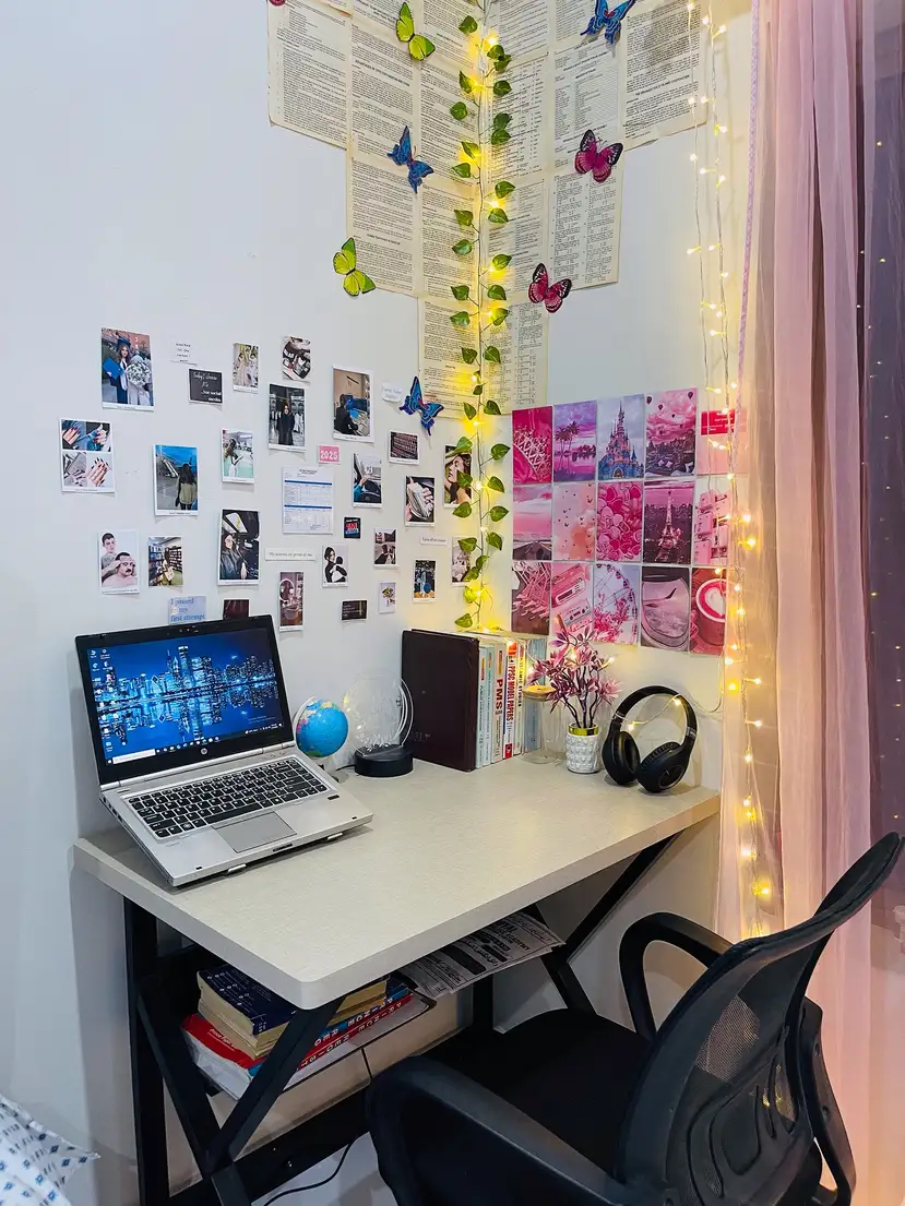 Small dorm desk with photo wall, colorful prints, butterflies, string lights, and open surface