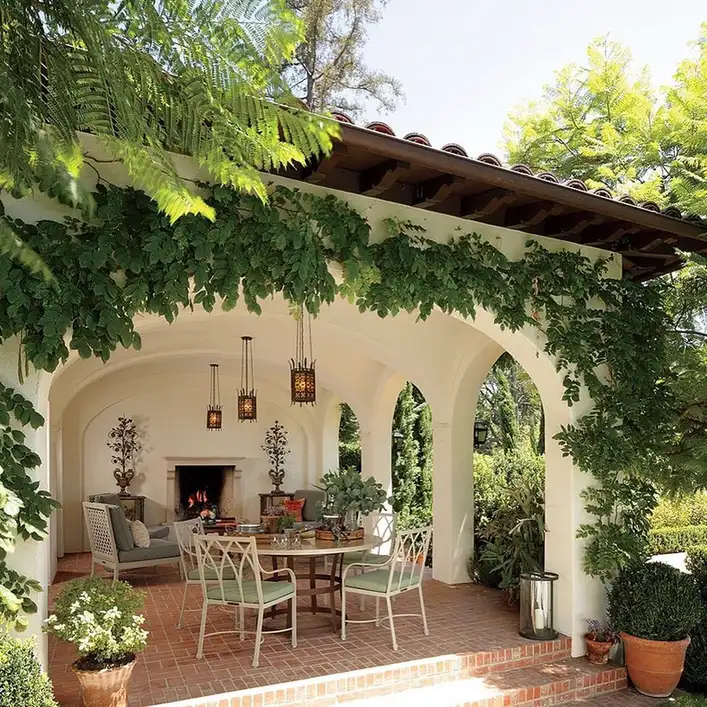 Covered porch with arched openings, wicker seating, climbing greenery, and outdoor rug