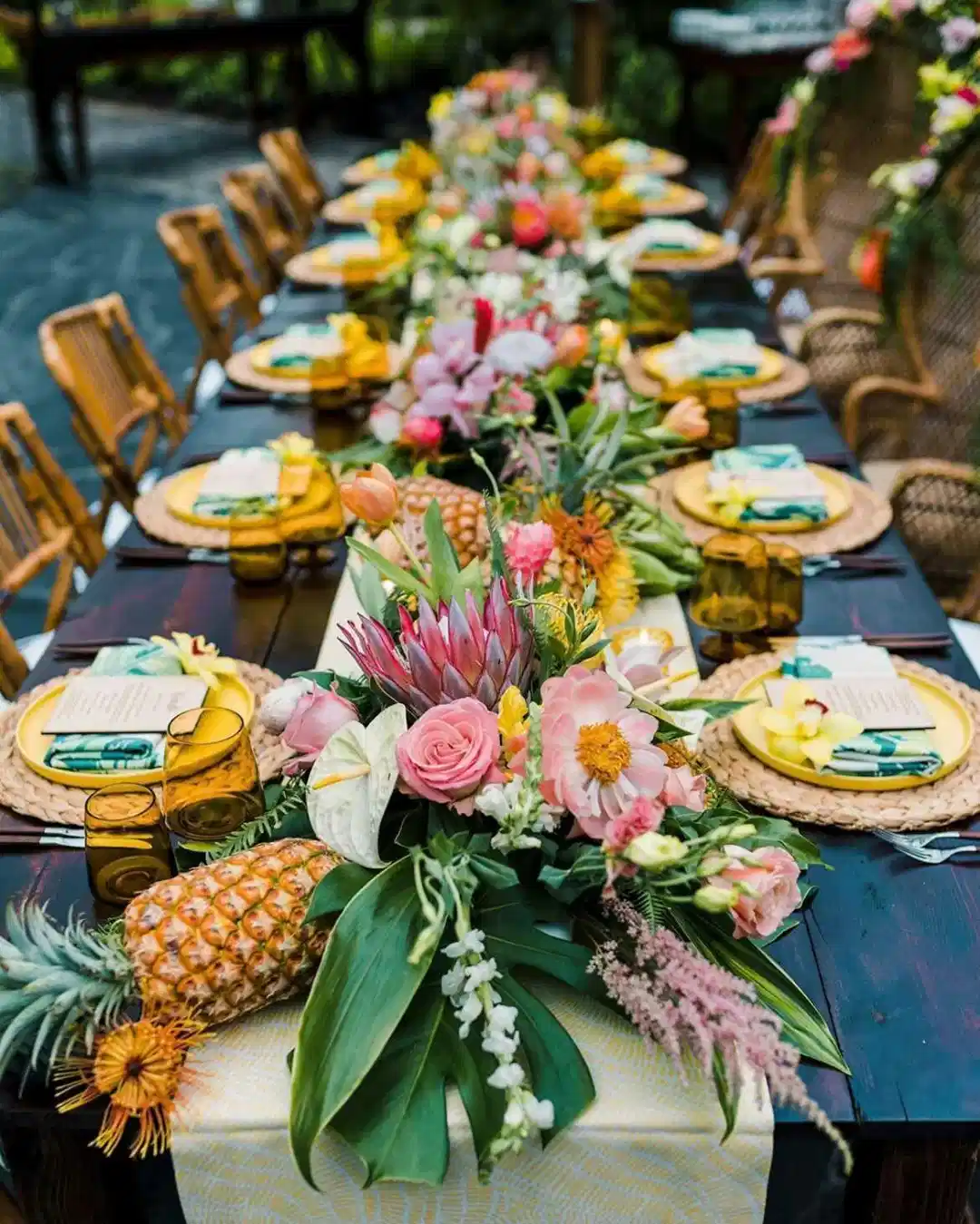 Tropical outdoor dining table decorated with bright flowers, leafy greenery, and tropical fruit
