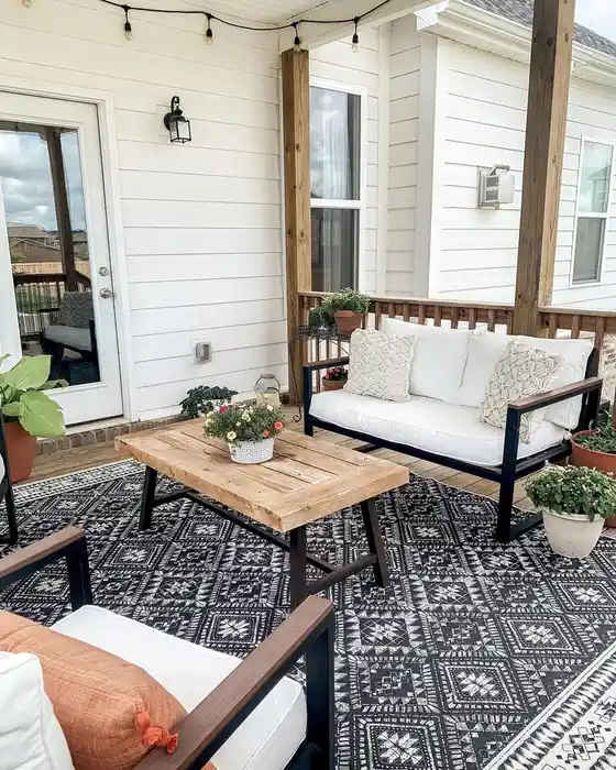 Muted patterned outdoor rug beneath a compact patio sofa and coffee table on a paved floor.