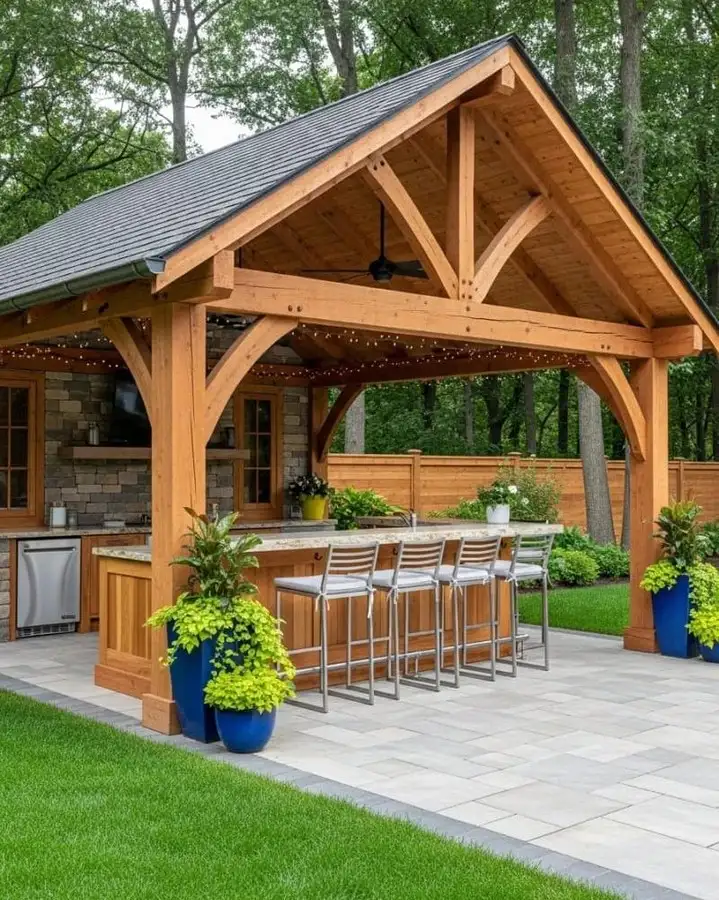 Covered outdoor kitchen with timber pavilion, long bar counter, wooden stools, and blue planters