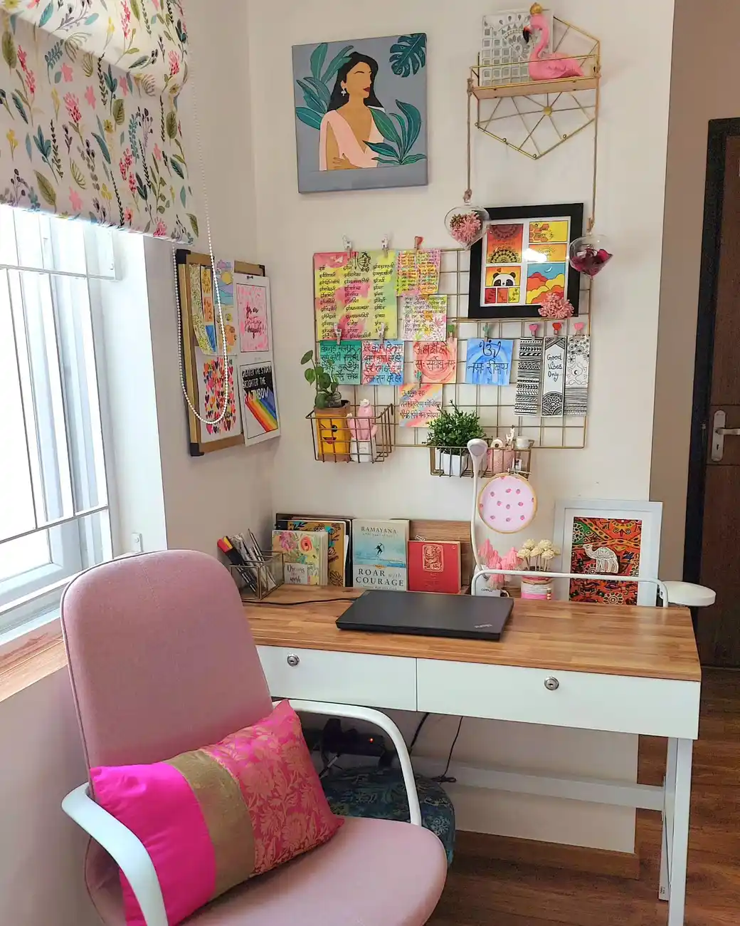 White and wood dorm desk with pink chair, colorful wall prints, notes, and cards