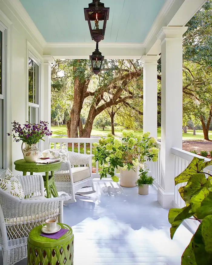 Green-themed covered porch with green ceiling, furniture, pendant light, plants, and white walls