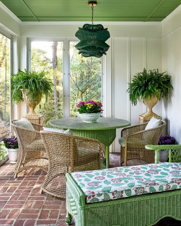 Garden room porch with wicker furniture, large windows, hanging plants, green pendant light, and brick floor