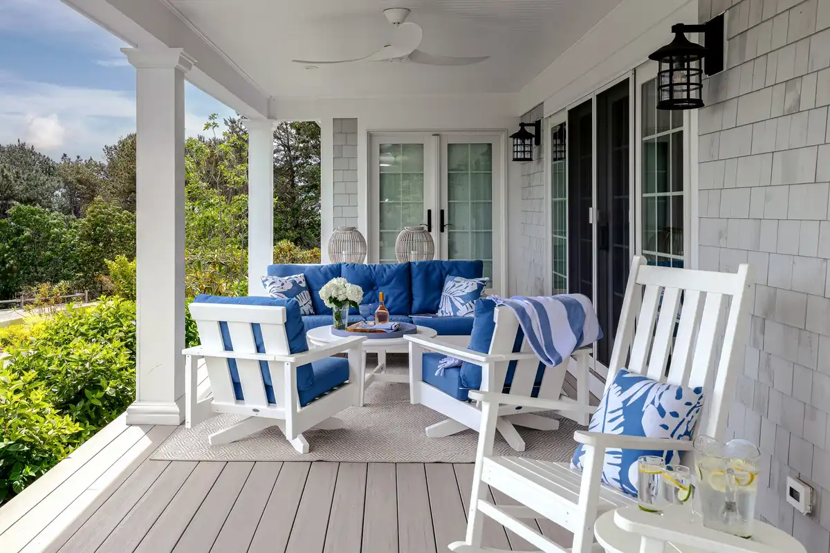 Covered porch with blue seating, patterned cushions, white columns, pale floor, and garden view