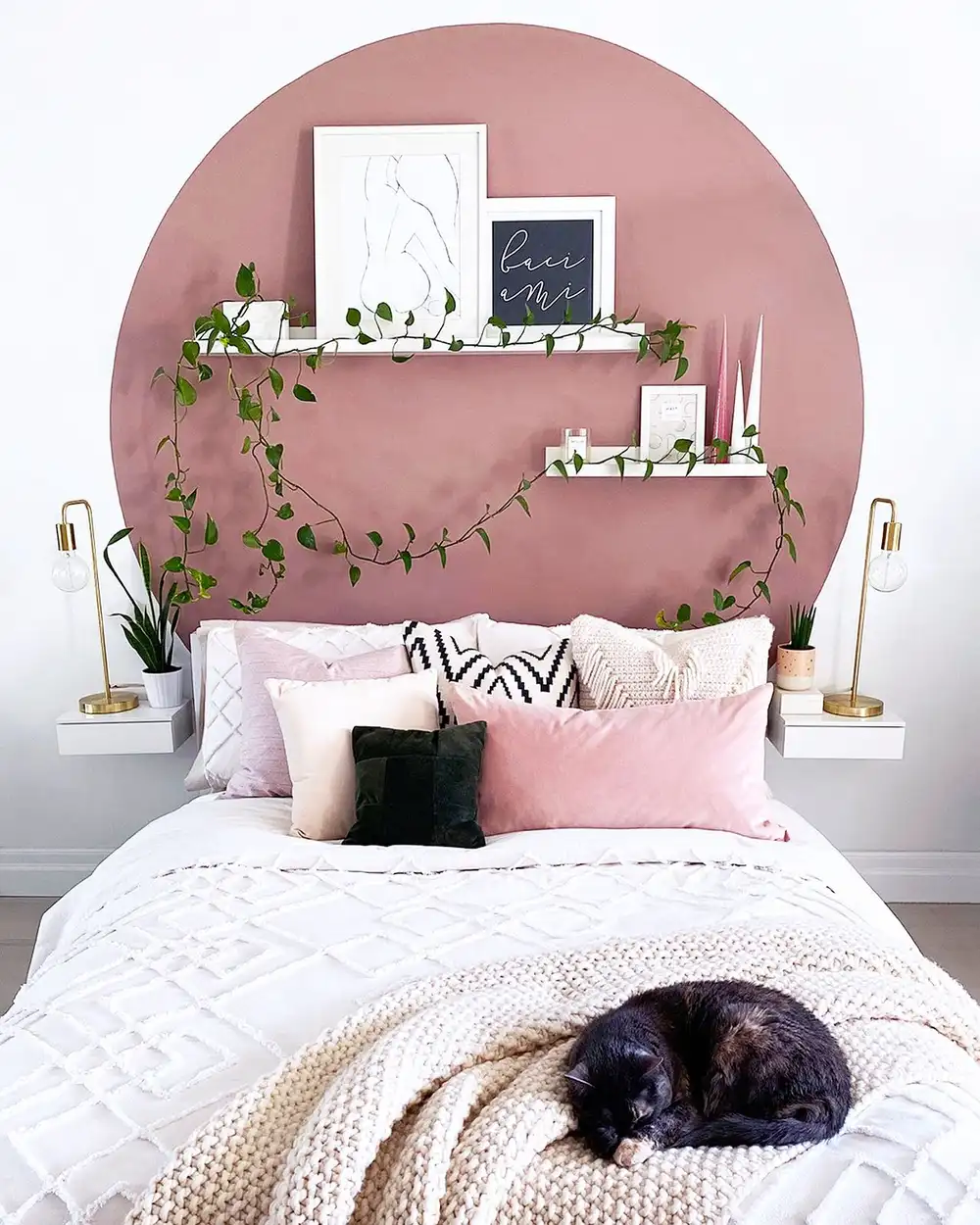 Small bedroom with large blush painted arch behind the bed, floating shelves and trailing plants