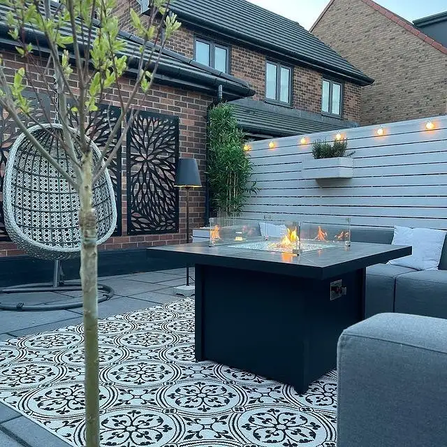 Light patterned outdoor rug on a dark deck with charcoal furniture and contrasting pale motifs.