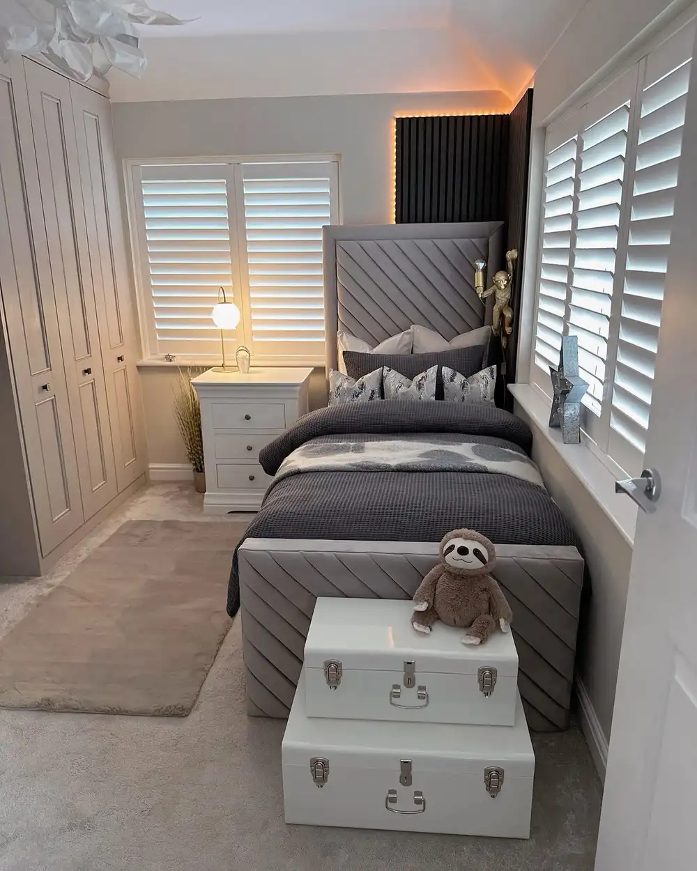 Narrow grey and white bedroom with built-in wardrobes, upholstered bed and dark slatted headboard wall