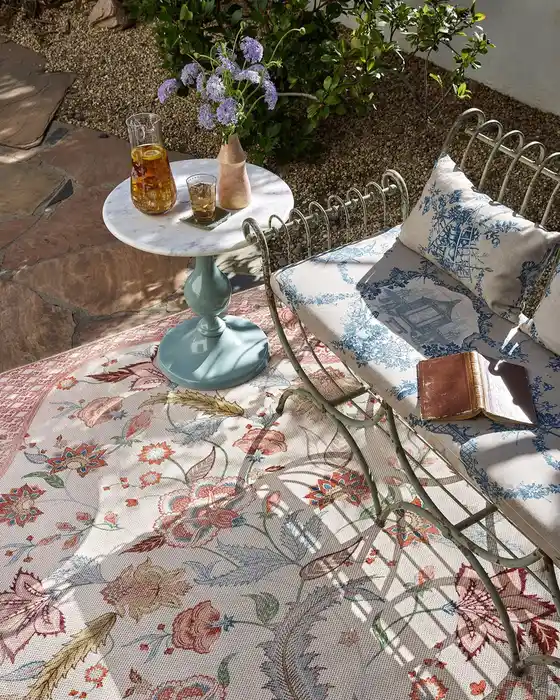 Faded floral outdoor rug with muted pink and earthy colors on a stone patio.