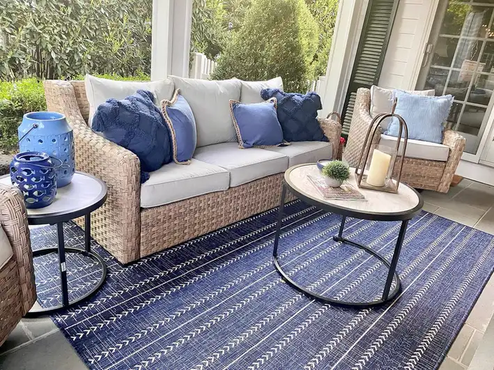 Covered porch with blue-and-white patterned rug, wicker seating, blue cushions, and round side tables