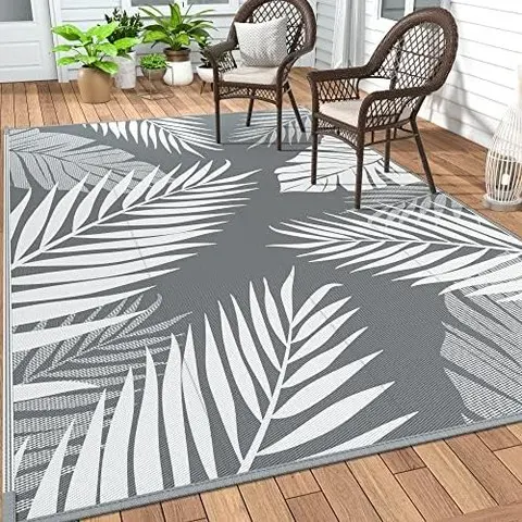 Gray outdoor rug with a bold white tropical leaf pattern on a wooden deck.