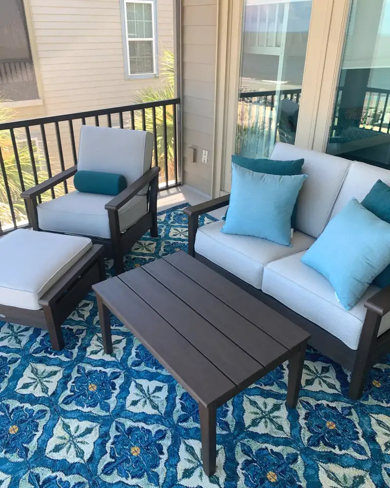 Rich blue geometric outdoor rug beneath pale blue seating on a small balcony.