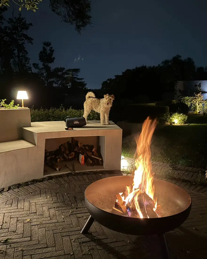 Round fire pit beside a built-in outdoor fireplace and patio seating