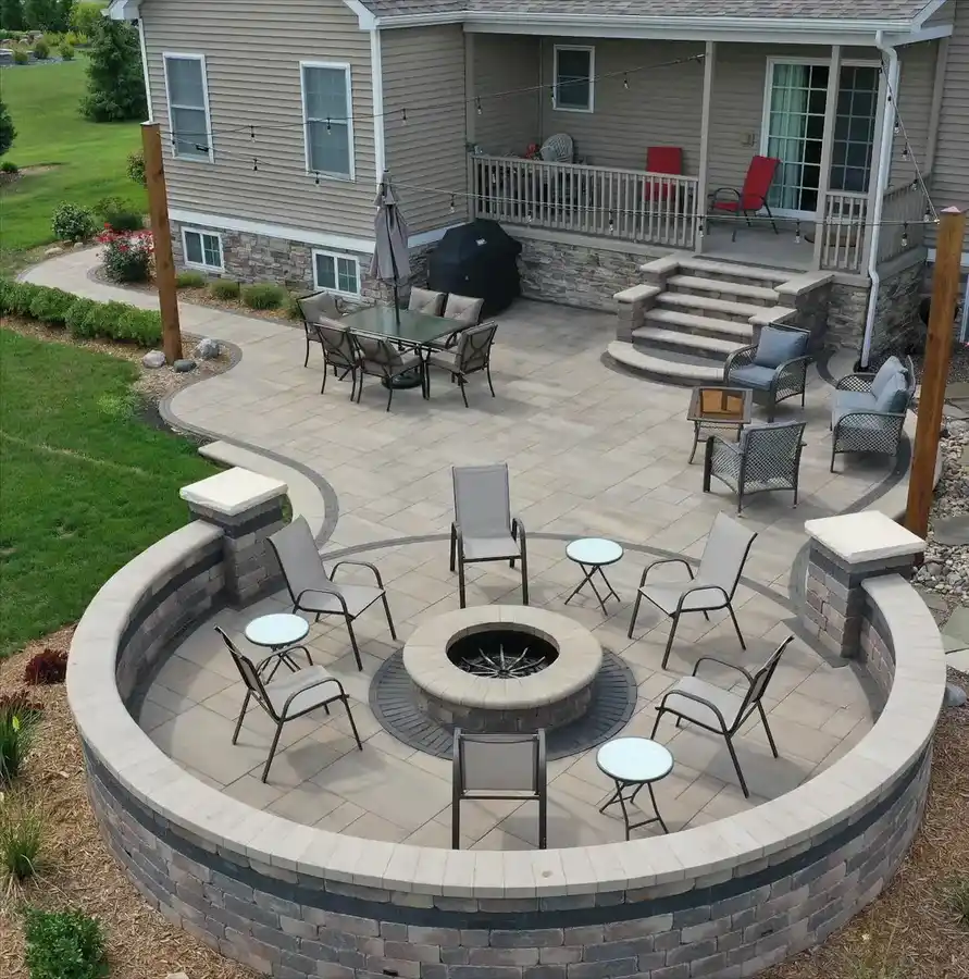 Round backyard fire pit on a raised circular stone patio with curved seating and outdoor chairs