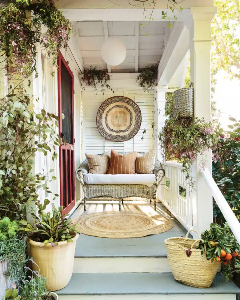 Small farmhouse porch with a wooden bench, round woven wall decoration, potted plants, and pale blue flooring