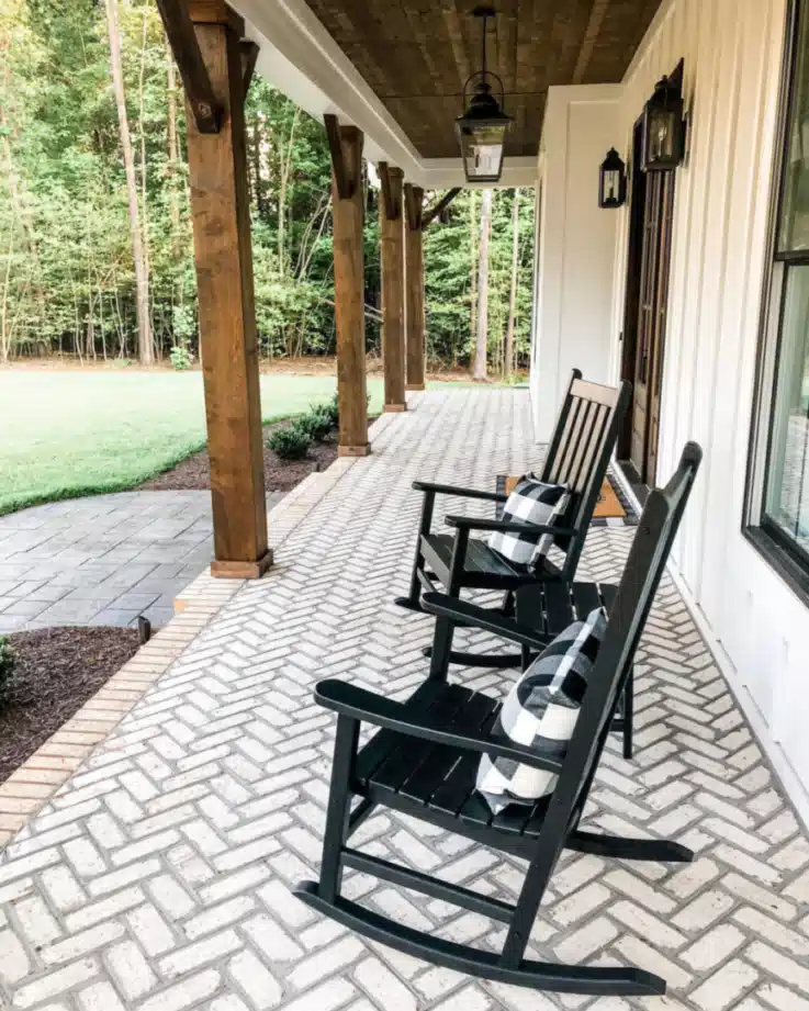 Long covered farmhouse porch with matching black rocking chairs, timber posts, and a brick floor