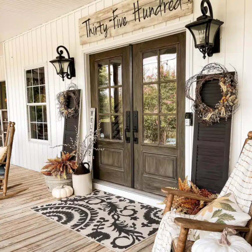 Farmhouse entrance with dark double doors, black lanterns, a patterned rug, and simple seating