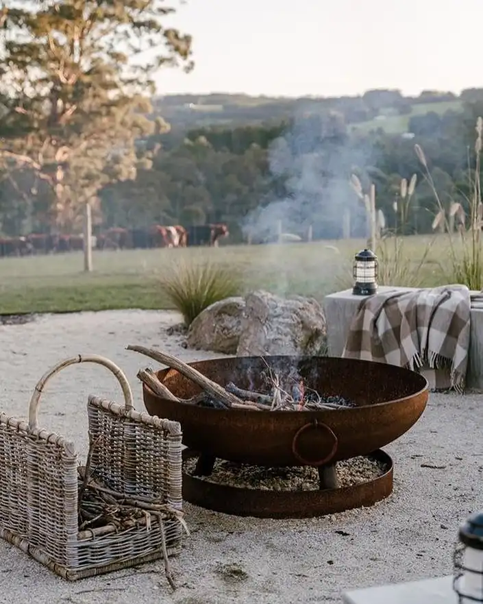 Rustic metal fire bowl on a gravel patio with simple outdoor chairs and an open landscape
